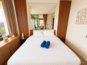 A hotel room with a large bed, a wooden headboard, a bedside table with a lamp, and a view of the outdoors. - Fully Seaview 2BR Apartment, Walk to Kamala Beach (Kamala)