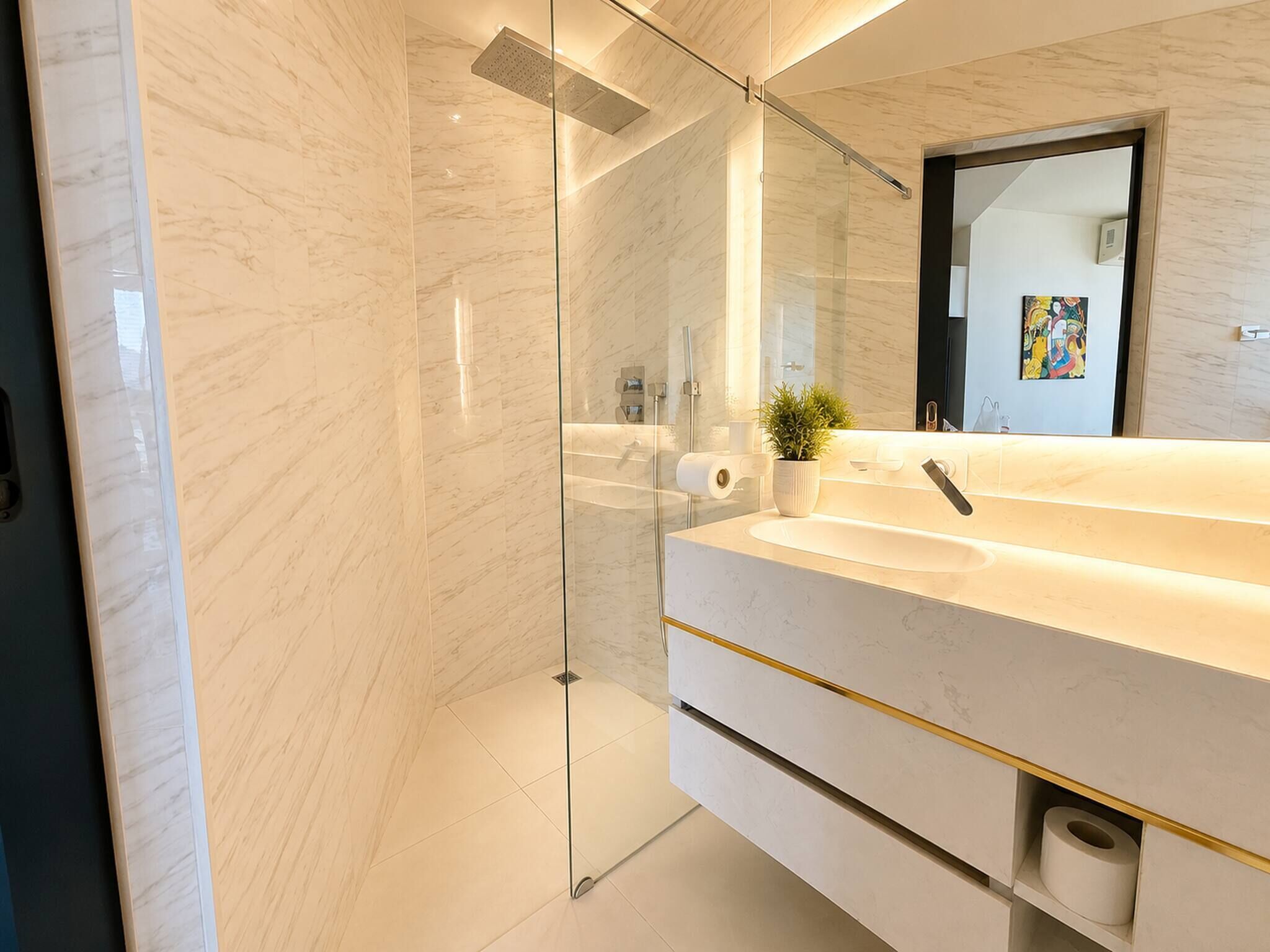 Ein modernes Badezimmer mit einer gläsernen Duschkabine, einem weißen Marmorwaschbecken und einem großen Spiegel.