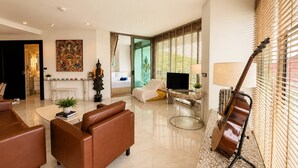 Ein modernes Wohnzimmer mit einem braunen Sofa, einem Glastisch und einer an der Wand angelehnten Gitarre.