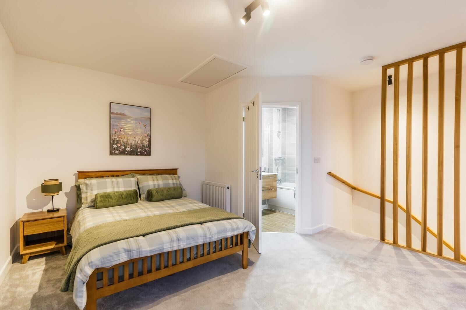 A bedroom with a bed, bedside table, lamp, and a painting on the wall.