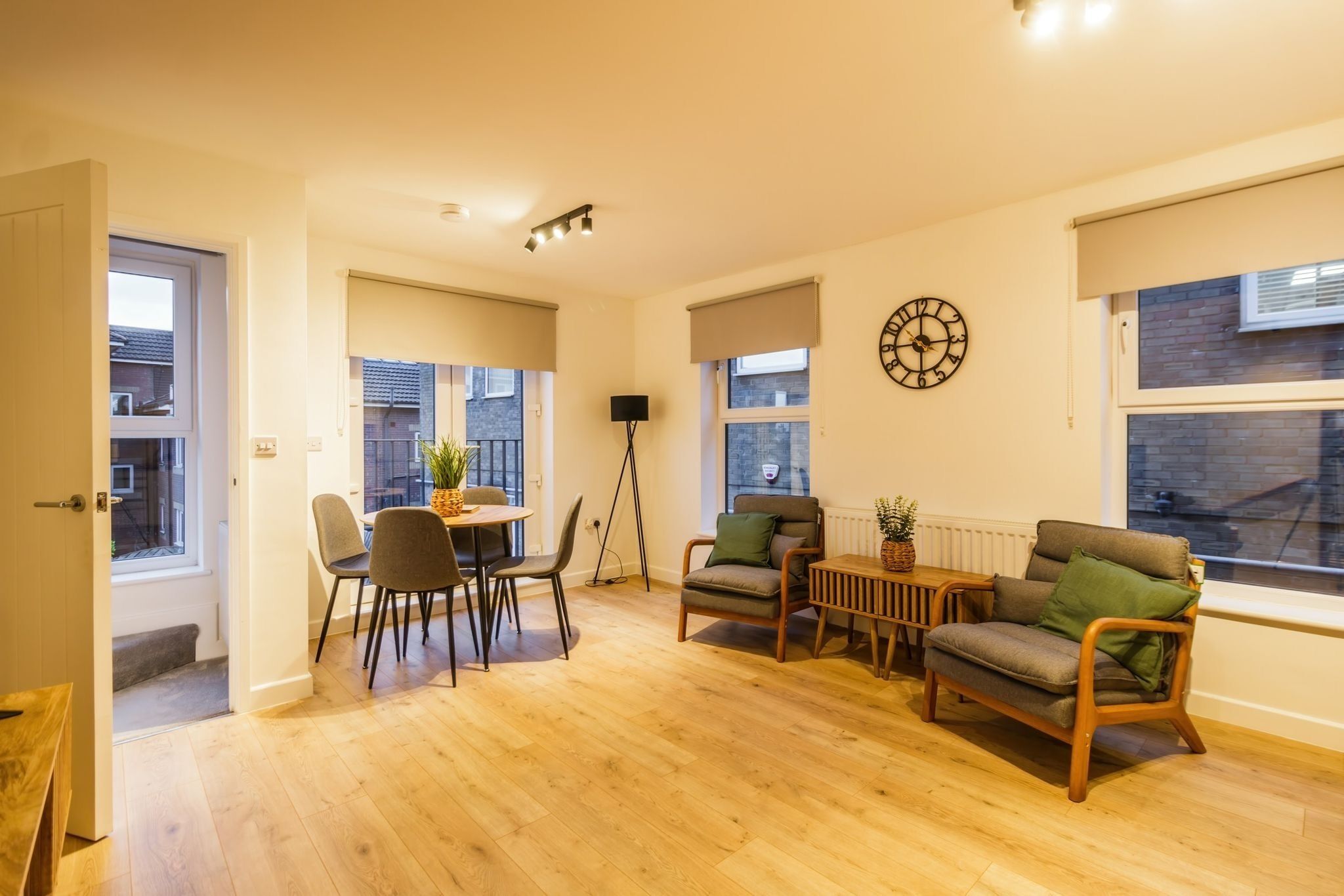 A spacious living area with a wooden floor, a dining table with chairs, a sofa, and a floor lamp.