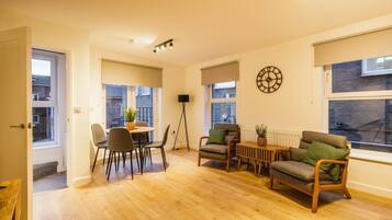 A spacious living area with a wooden floor, a dining table with chairs, a sofa, and a floor lamp.