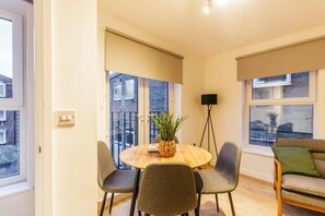 Ein modernes Wohnzimmer mit einem runden Holztisch, grau gepolsterten Sesseln, einer Stehlampe und einem Sofa mit einem grünen Kissen.