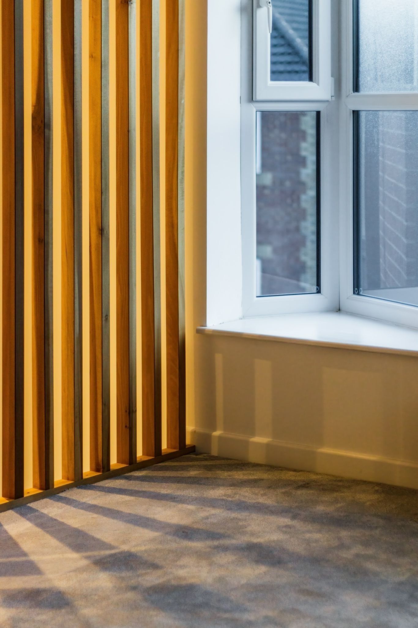 A corner of a room with a window, a wooden slat wall, and a carpeted floor.
