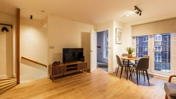 A modern living room with a wooden floor, a TV stand, and a dining area with chairs.
