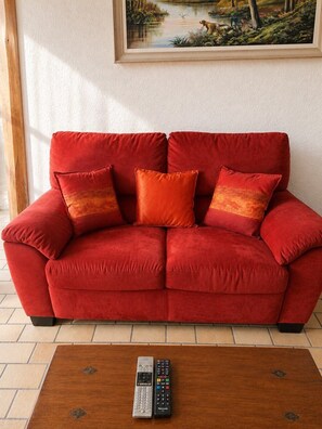 A red sofa with three cushions and a remote control on a wooden coffee table. - Getaway in Touraine–House with a private courtyard (Bléré)