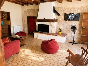 A cozy living room with a fireplace, a television, a dartboard, and a fan. - Getaway in Touraine–House with a private courtyard (Bléré)