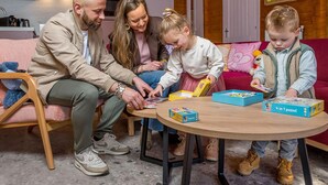 A family engaged in a puzzle activity in a cozy room with wooden walls, a round table, and a sofa.