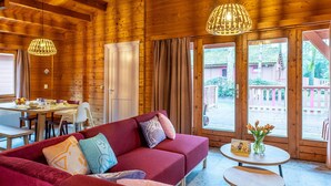 A wooden interior with a sofa, dining table, and a view through large windows.