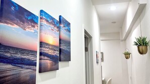 Passadís amb parets blanques, un sòl de fusta i tres quadres amb una posta de sol sobre l'oceà.
