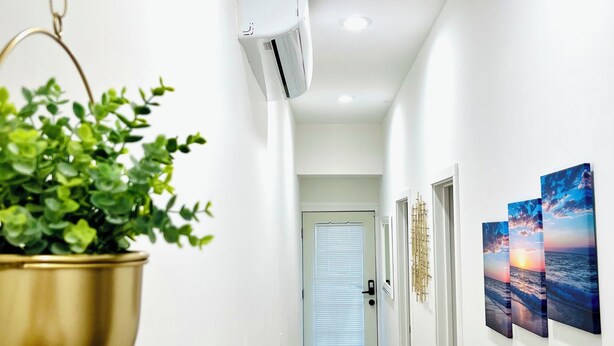 Passadís amb una planta penjant, un aparell d'aire condicionat, una porta amb una finestra i una paret amb tres quadres emmarcados.