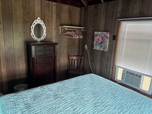 A bedroom with a wooden wall, a dresser, a chair, a bed with a quilt, a mirror, a clothes rack, and a window with blinds. - 3 bedroom Beach House central to food and shops, steps away from the ocean. (Old Lyme)
