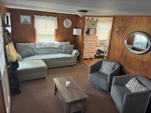 Ein gemütliches Wohnzimmer mit einer Couch, zwei Sesseln, einem Couchtisch, einer Uhr und einem Spiegel.