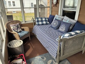 A cozy room with a bed, a wicker chair, and a small table. - 3 bedroom Beach House central to food and shops, steps away from the ocean. (Old Lyme)