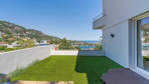 Ein moderner Balkon mit Blick auf eine Küstenstadt und eine Rasenfläche.