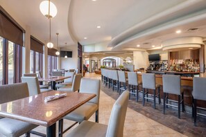 Ein modernes Restaurant mit Barbereich, Marmortischen und -stühlen sowie einem gut beleuchteten Innenraum.
