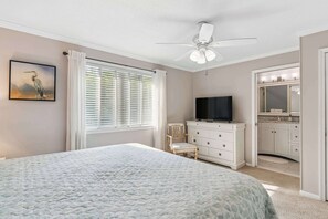 Ein Schlafzimmer mit Bett, Fernseher, Kommode und einem Badezimmer mit Spiegel und Waschbecken.