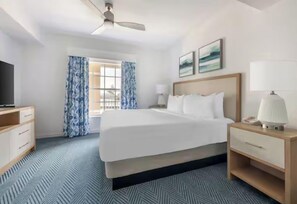 Ein Hotelzimmer mit einem großen Bett, einem Nachttisch mit Lampe, einem Fernseher und einem Fenster mit Vorhängen.