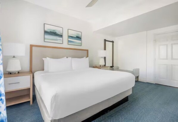 Ein Hotelzimmer mit einem großen Bett, zwei Nachttischen mit Lampen, einem Sessel und zwei abstrakten Bildern an der Wand.