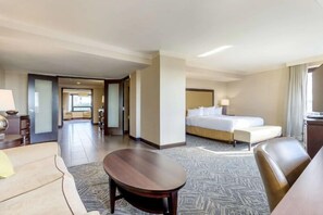 Habitación de hotel con cama, sofá, una mesita y vistas al pasillo.