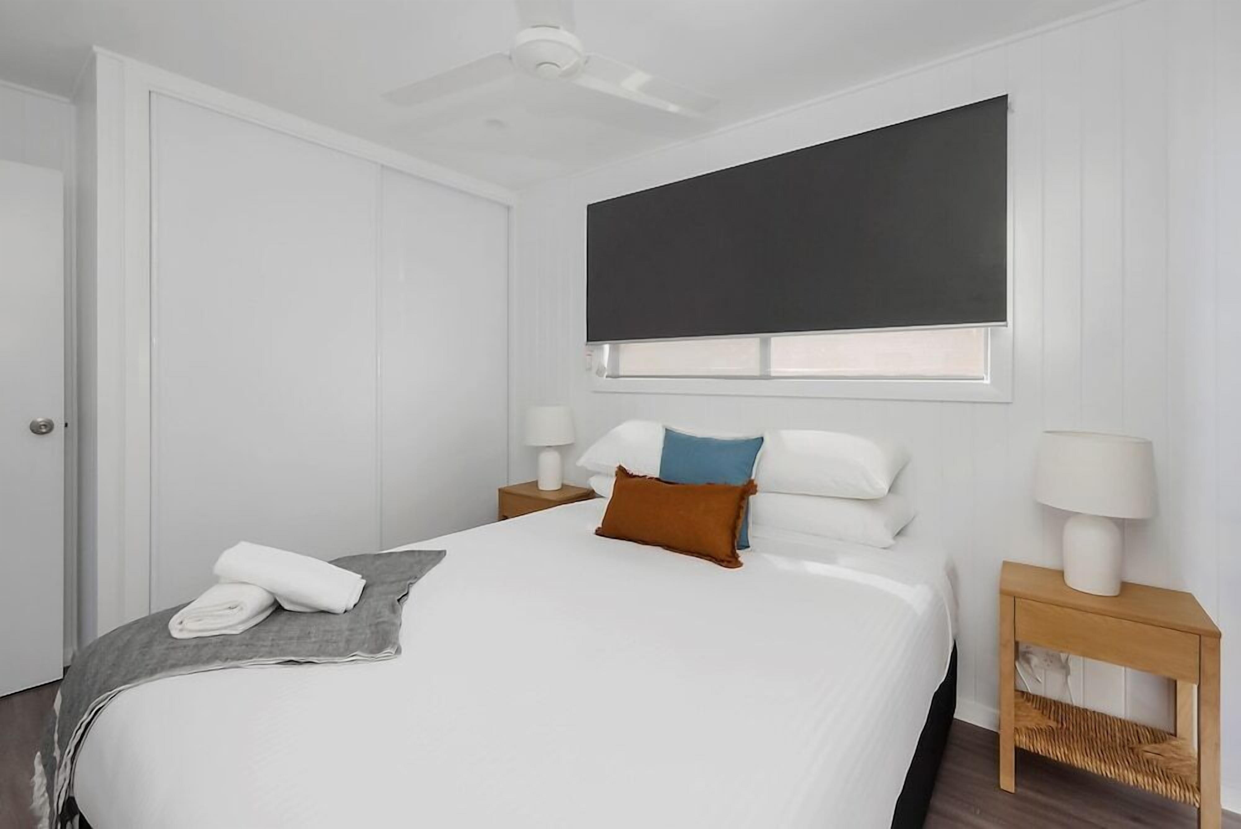 Una camera d'albergo con un letto, due comodini, una ventola a soffitto, una finestra con una tenda e una porta.