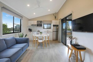 A modern kitchen with white cabinets, a dining table with chairs, a sofa, and a flat-screen TV mounted on the wall. - Reflections Holiday Park Forster Beach (Forster)