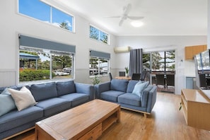 A modern living room with a sofa set, a wooden coffee table, and a dining area with chairs. - Reflections Holiday Park Forster Beach (Forster)