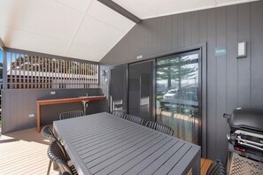 A covered outdoor dining area with a table and chairs, a grill, and a sliding glass door. - Reflections Holiday Park Forster Beach (Forster)