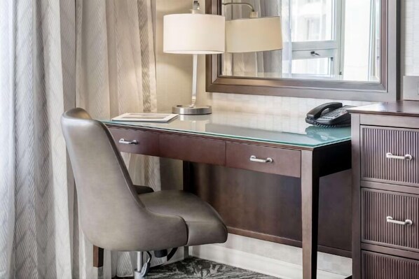 Ein Hotelzimmer mit Schreibtisch, Stuhl, Lampe, Telefon und Spiegel.