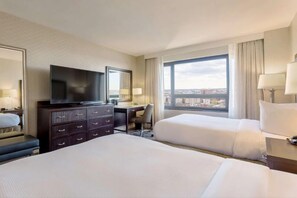 Habitación de hotel con dos camas, un escritorio, televisión y un amplio ventanal con vistas a la ciudad.