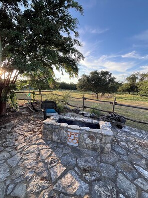 A stone patio with a fire pit, surrounded by a fence and trees. - Cottage on Exotic Animal Ranch -- Weekend Retreat in Texas Hill Country (Driftwood)