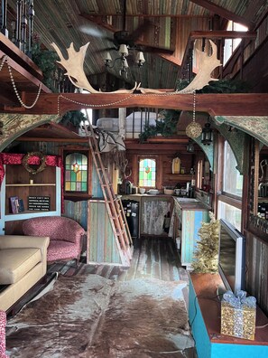 A rustic interior with a wooden ceiling, a staircase, a kitchen area, and a seating area with a decorative wall. - Cottage on Exotic Animal Ranch -- Weekend Retreat in Texas Hill Country (Driftwood)