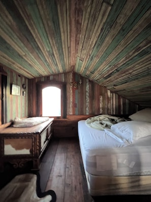 A rustic attic bedroom with a wooden ceiling, a single bed, a nightstand, and a window. - Cottage on Exotic Animal Ranch -- Weekend Retreat in Texas Hill Country (Driftwood)
