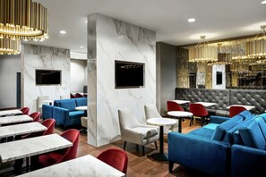 Un interior de restaurante moderno con paredes de mármol, asientos en rojo y azul, y candelabros dorados.