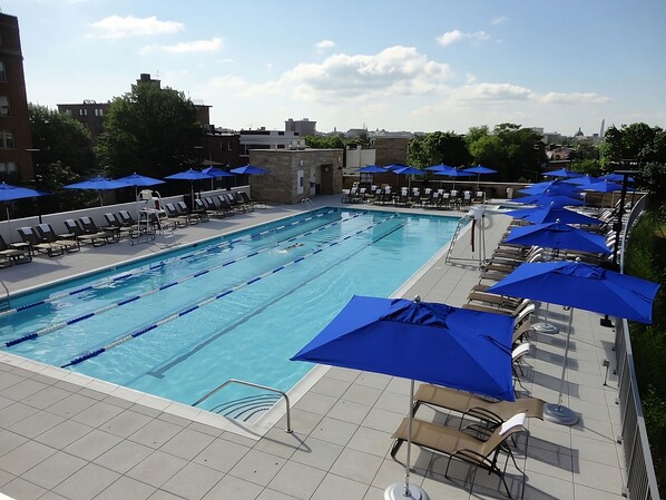 Ein Schwimmbecken mit mehreren Bahnen, Liegestühlen und blauen Sonnenschirmen.