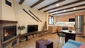 Ein modernes Wohnzimmer mit Kamin, Fernseher und Küchenbereich mit Holzschränken und Kühlschrank.