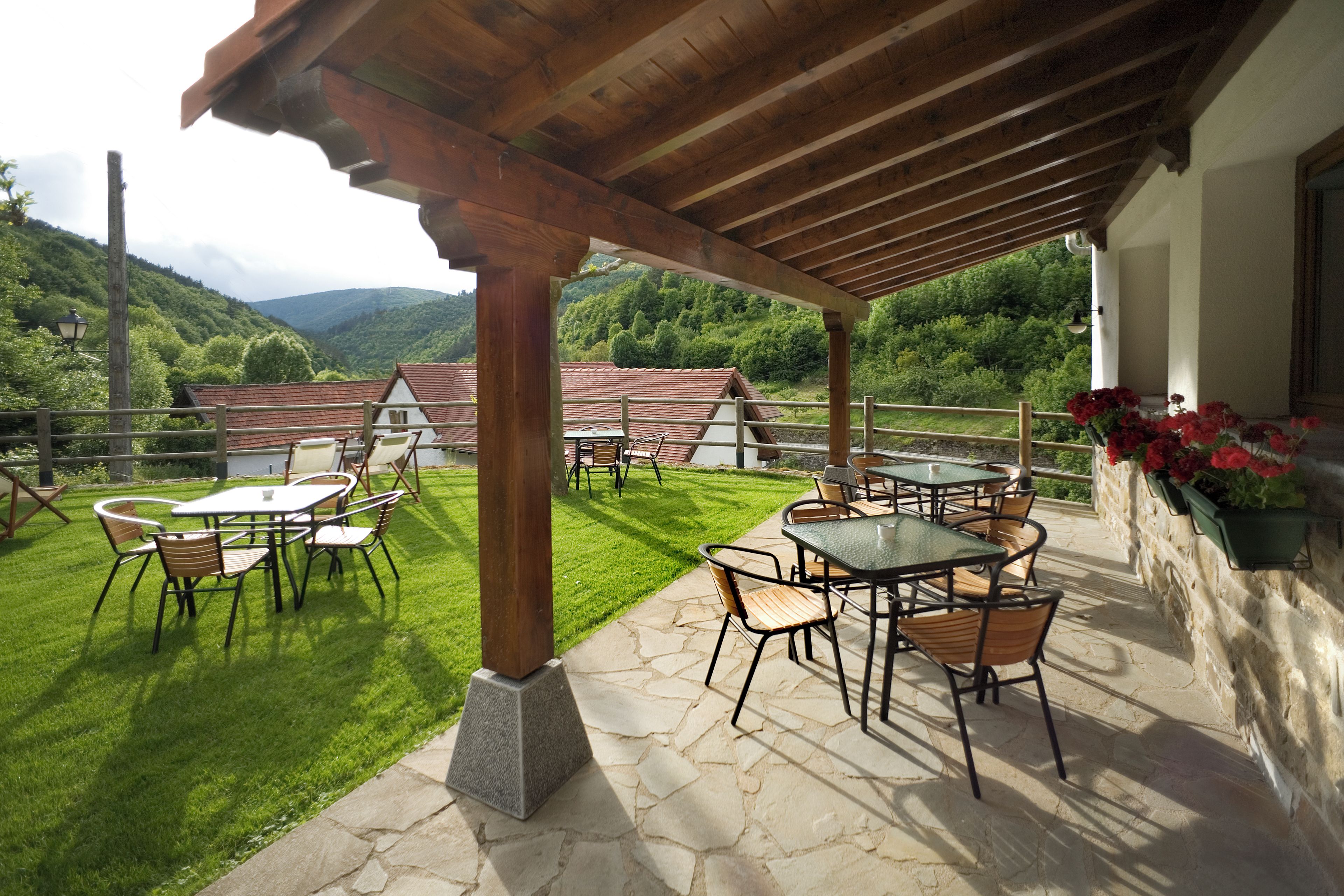 Een terras buiten met tafels en stoelen, een stenen vloer en uitzicht op het omliggende landschap.