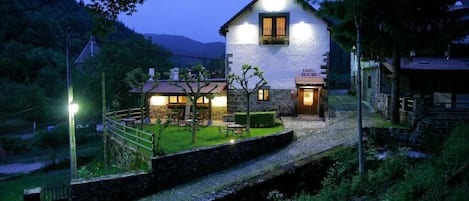 A two-story stone building with a well-lit entrance and a small outdoor seating area.