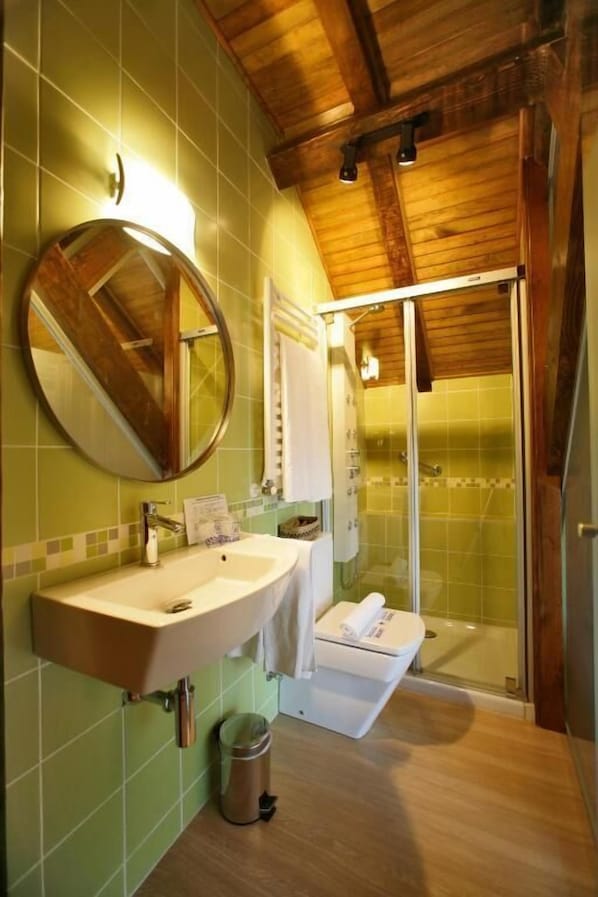 A bathroom with a wooden ceiling, a round mirror, a sink, a toilet, and a glass shower enclosure. - Hotel Rural Besaro - Selva de Irati (Izalzu)
