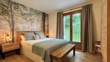 Una camera da letto con un letto, una panca, un comodino, un affresco sulla parete, una finestra con tende e vista sul verde circostante.