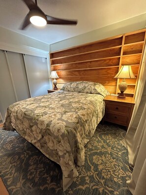 Ein Schlafzimmer mit einem Bett, zwei Nachttischen, einem Deckenventilator und einem gemusterten Teppich.