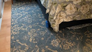 Une chambre à coucher avec une tête de lit en bois, un lit recouvert d’une literie à motifs floraux, deux tables de chevet avec des lampes, une petite commode et un tapis à motifs.