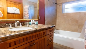 Un baño con encimera de granito, dos lavamanos, un espejo grande y una bañera.