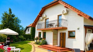 A two-story house with a balcony, a patio with outdoor furniture, and a well-maintained garden. - Studio for 2 People Near the sea (Kamien Pomorski)