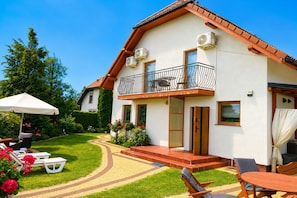 A two-story house with a balcony, a patio with outdoor furniture, and a well-maintained garden. - Studio for 2 People Near the sea (Kamien Pomorski)
