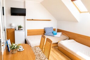 A compact bedroom with two single beds, a wooden headboard, a small table with a plant, and a television mounted on the wall. - Studio for 2 People Near the sea (Kamien Pomorski)