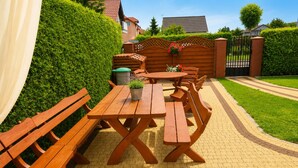A wooden picnic table set on a paved patio with benches, surrounded by a well-maintained hedge and a gated entrance. - Studio for 2 People Near the sea (Kamien Pomorski)