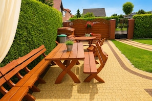 A wooden picnic table set on a paved patio with benches, surrounded by a well-maintained hedge and a gated entrance. - Studio for 2 People Near the sea (Kamien Pomorski)