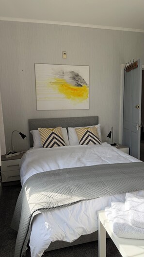 A neatly made bed with a gray headboard, a bedside table with a lamp, and a wall-mounted artwork.