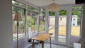 A conservatory with a table and chairs, large windows, and a hanging light fixture. - Cute cottage for 8, near city centre, parking, gardens. Newly refurbished. (Edinburgh)